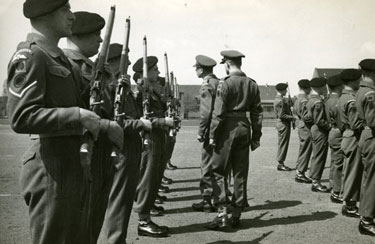 Captain R G Clutterbuck accompanied by 2nd Lieutenant Saunders (Guard Commander) inspecting the rifles of the Guard in the parade ground before marching off.