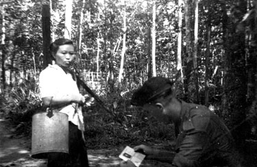 Unidentified soldier examining identity card of rubber tapper